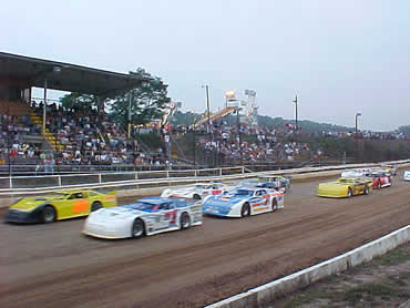 Super late Model Heat race action w/ fair rides in background